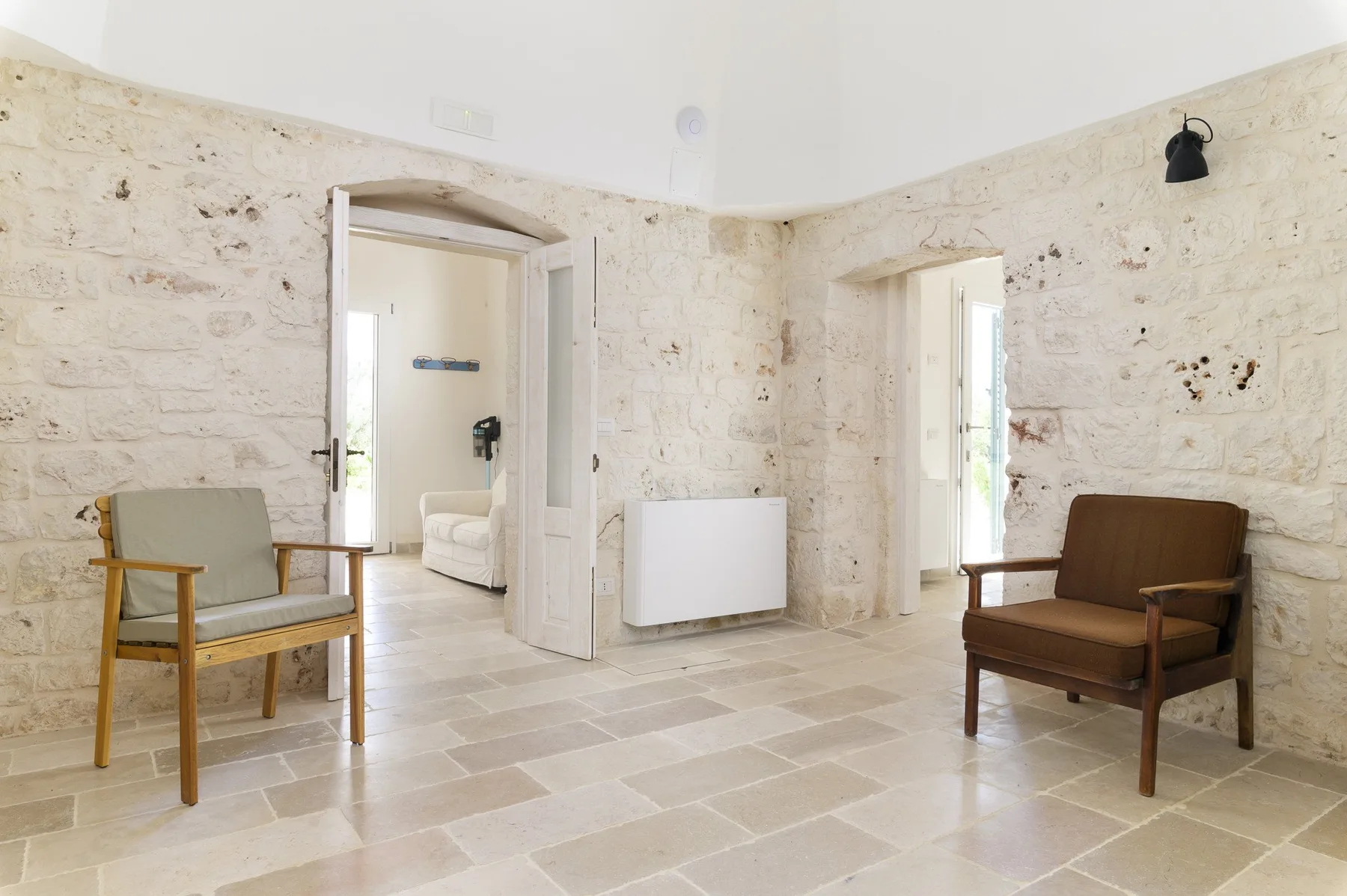 Una luminosa habitación de paredes de piedra con dos sillones y puertas abiertas.