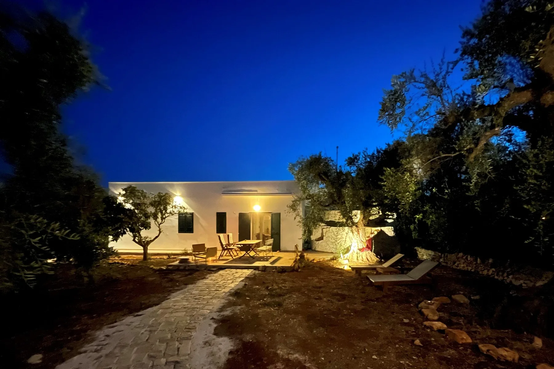 Un edificio iluminado y una zona de asientos al aire libre junto a un sendero de piedra al anochecer.
