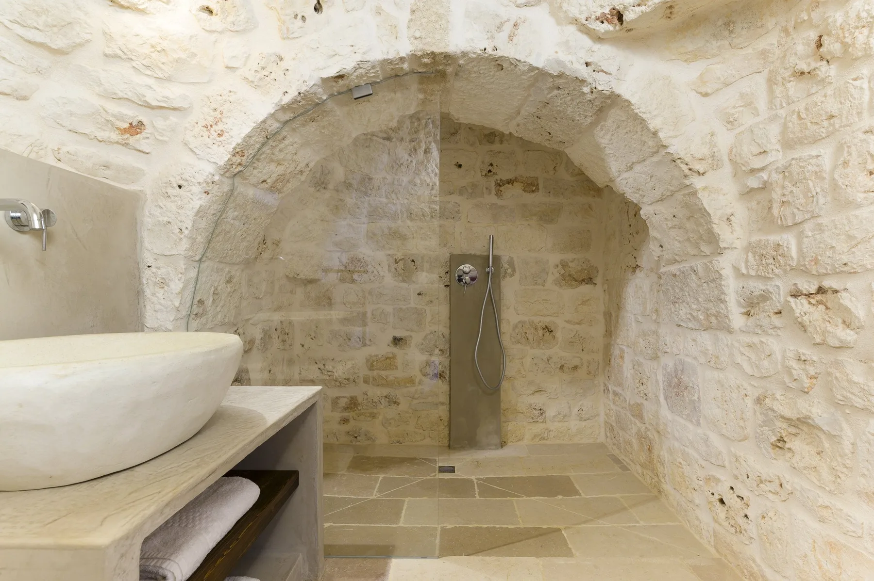 Un baño de piedra con una ducha de pared y un lavabo sobre una encimera.