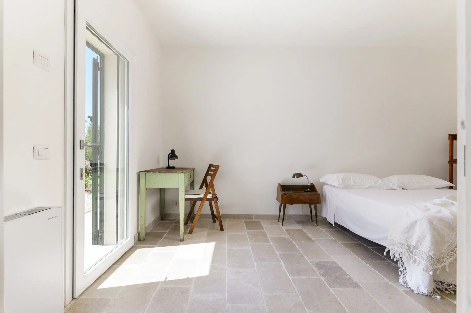 Un dormitorio luminoso con una cama, un escritorio pequeño y una silla.