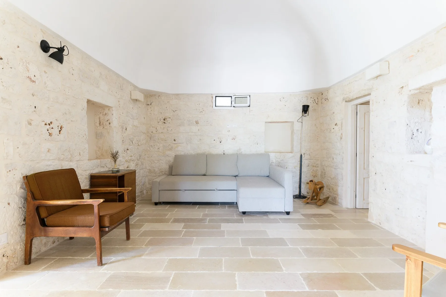 Una luminosa sala de estar con paredes de piedra, un sofá seccional y un sillón de madera.
