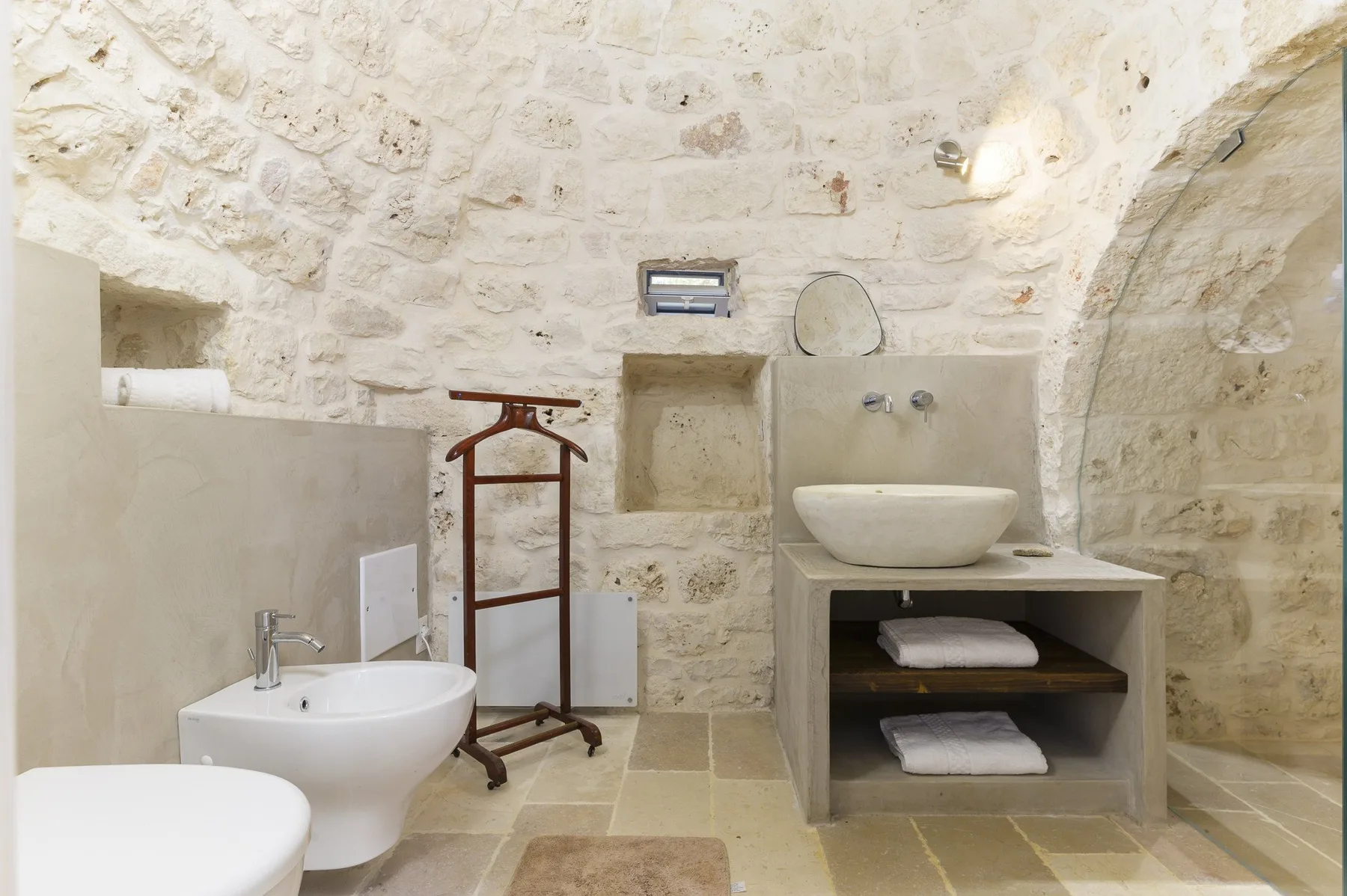 Un baño de piedra con lavabo, zona de ducha y toallero.