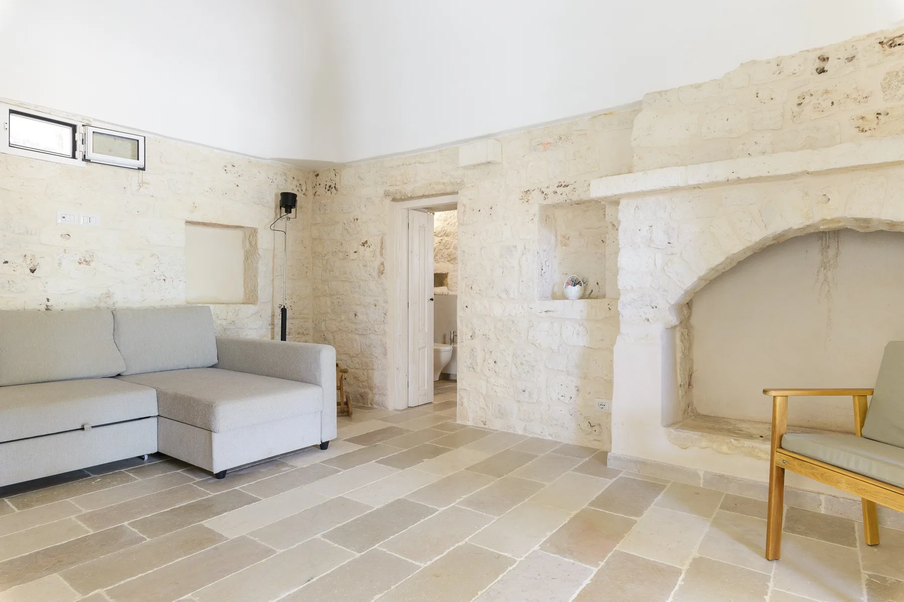 Una luminosa sala de estar de piedra con asientos claros y un gran nicho arqueado en la pared.