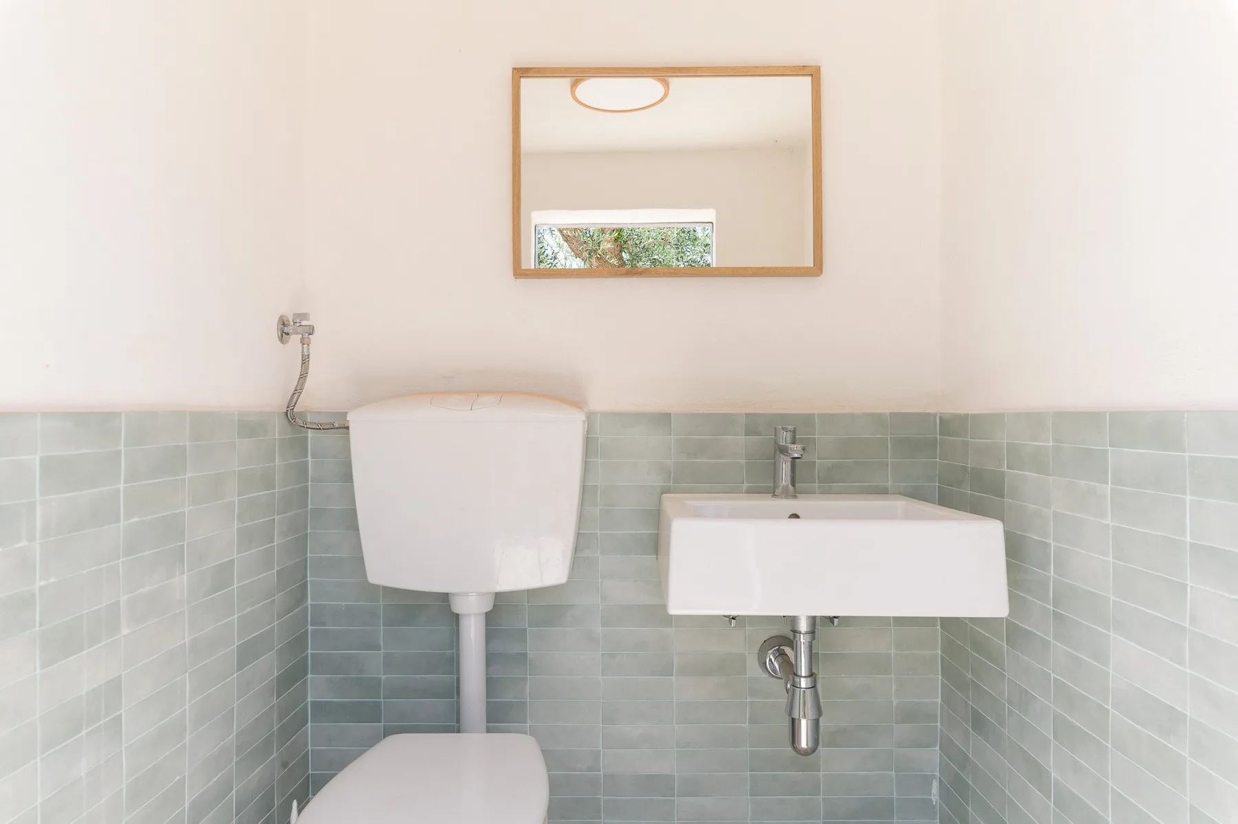 Un baño con inodoro, lavabo de pared y espejo rectangular.