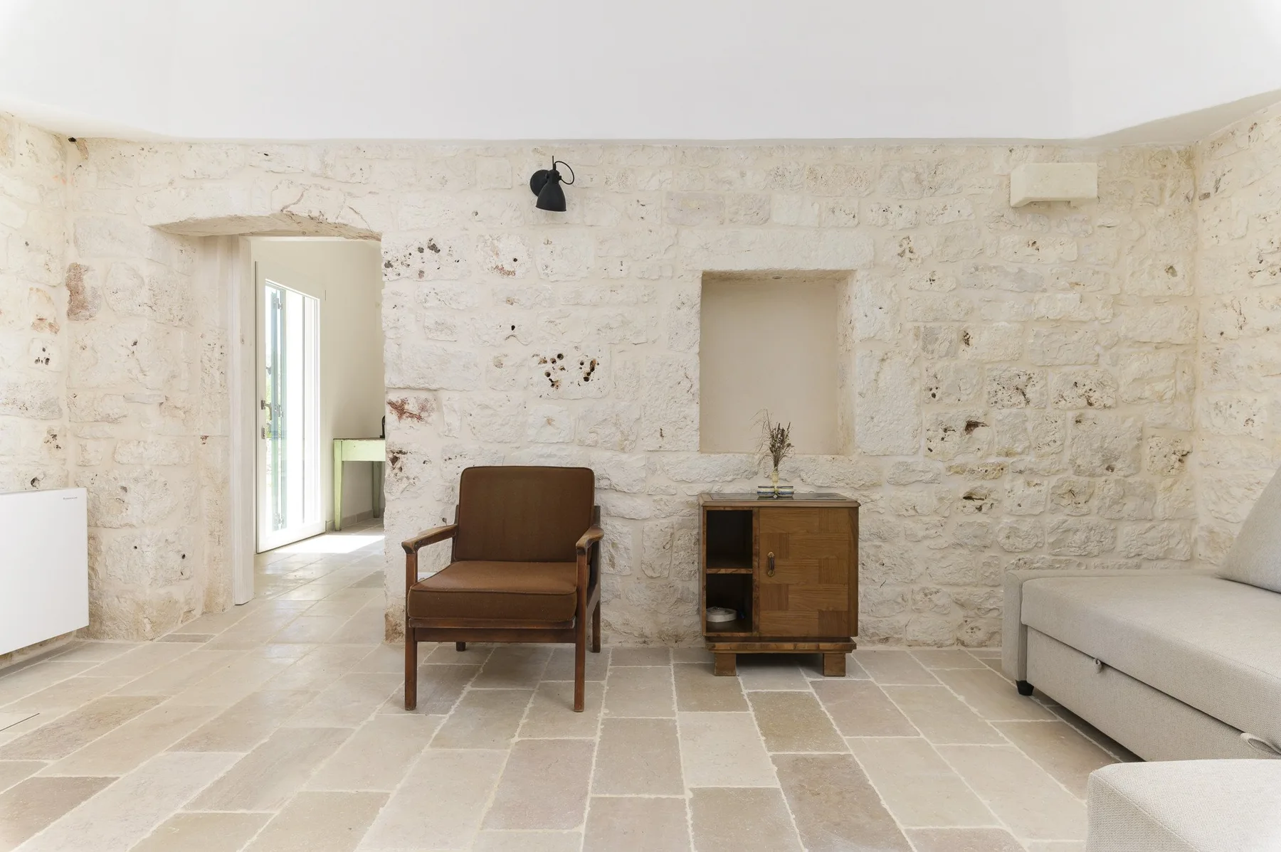 Una sala de estar con paredes de piedra, una silla de madera y un mueble bajo.