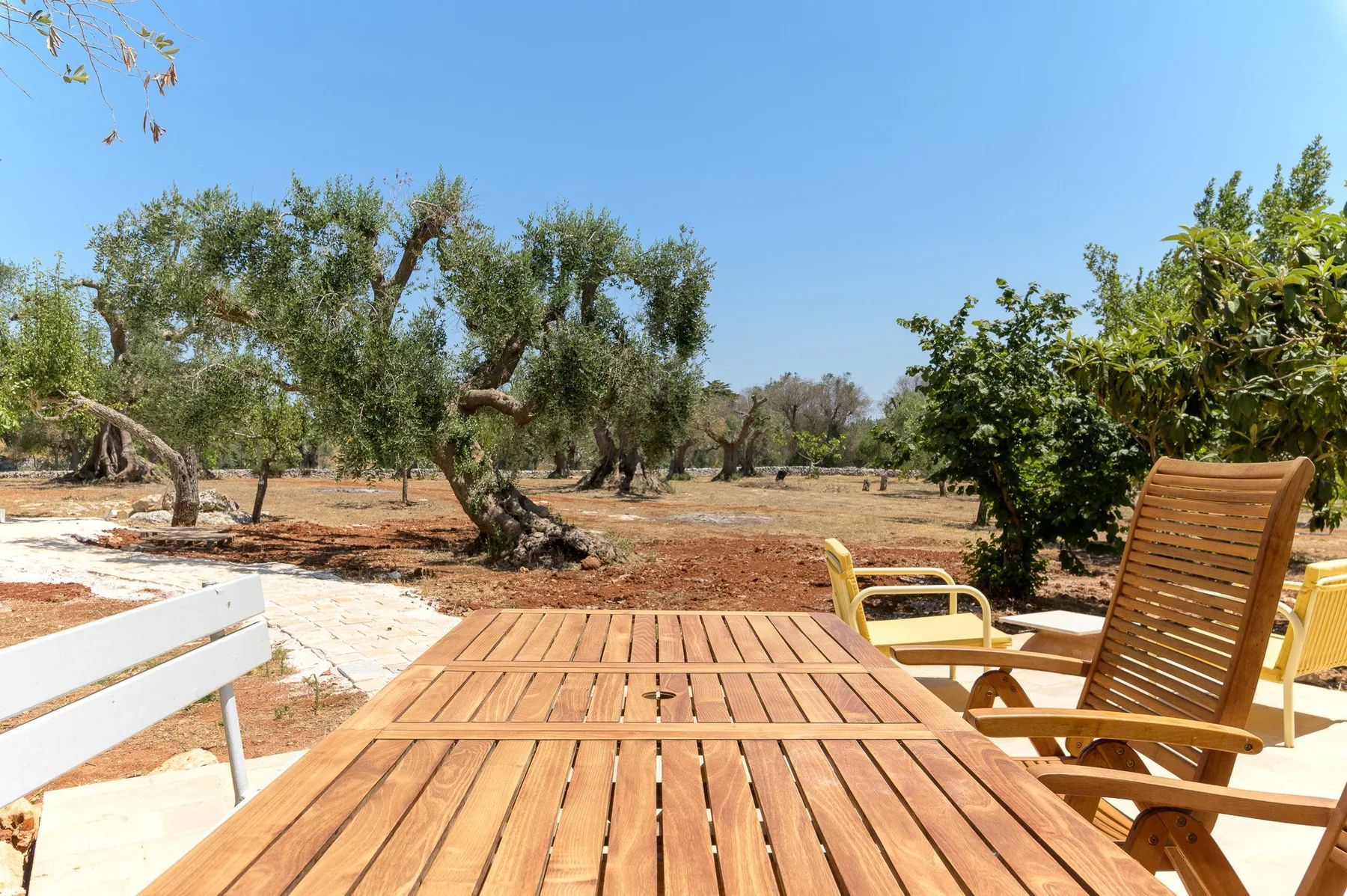 Un patio al aire libre con una mesa y sillas de madera da a un paisaje arbolado.