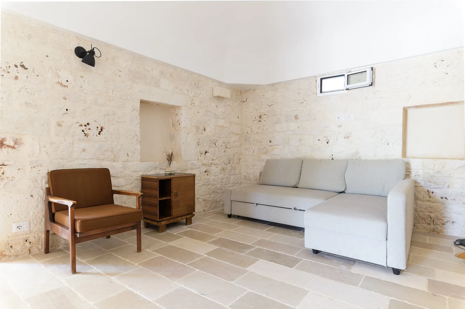 Una sala luminosa con paredes de piedra, un sofá y un sillón.