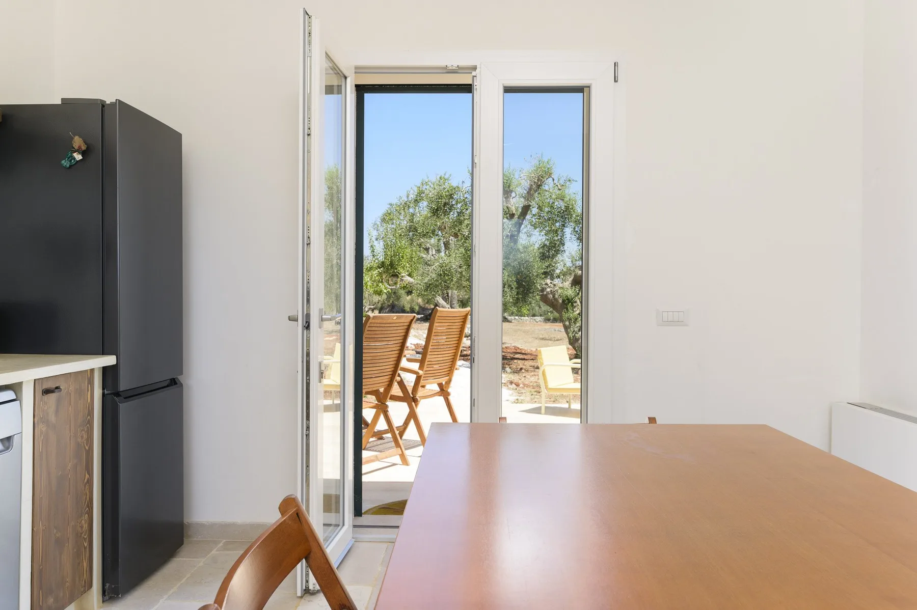 Un comedor con una mesa de madera junto a puertas de vidrio abiertas hacia un patio.