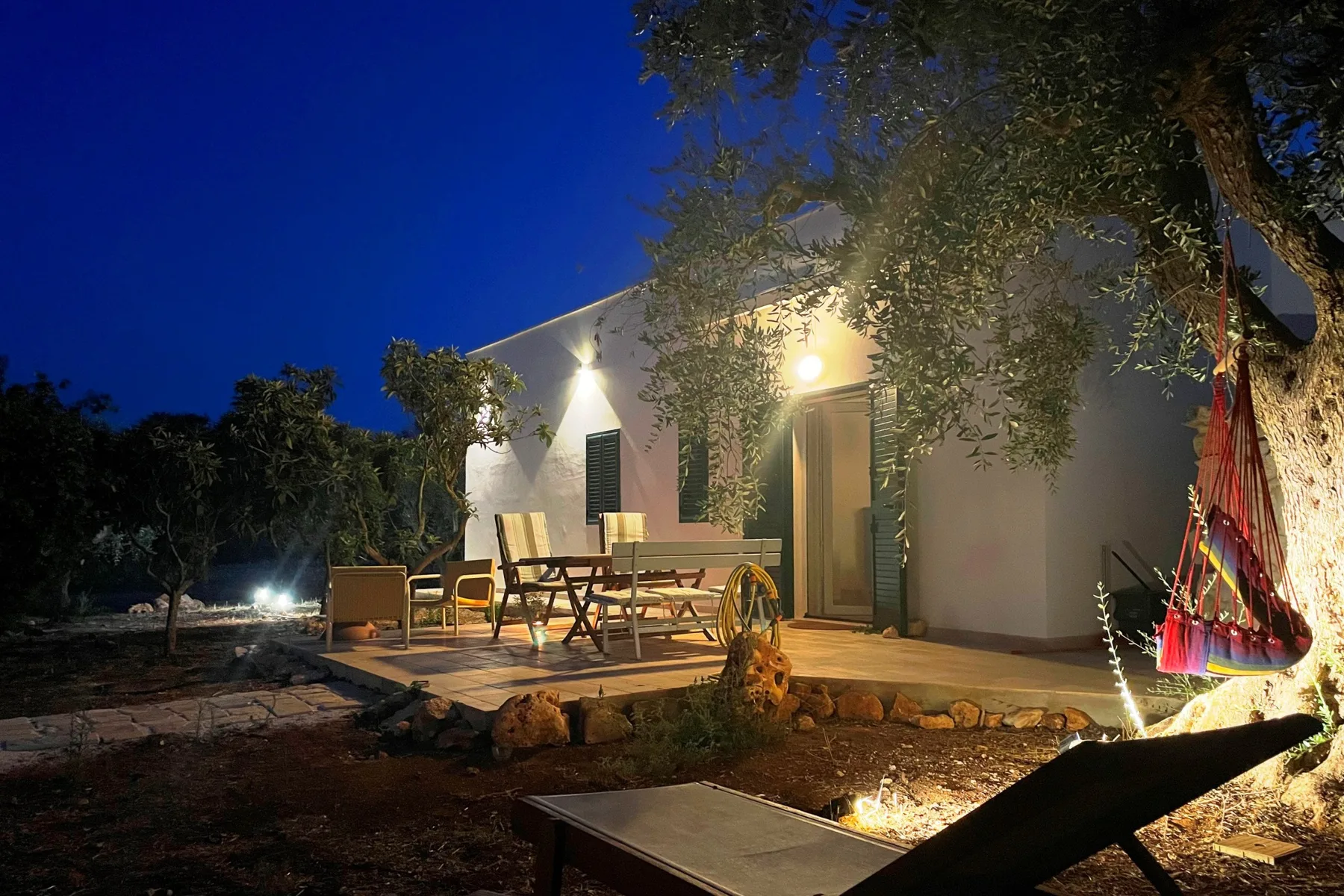 Una zona de estar al aire libre junto a una casa, iluminada al anochecer.
