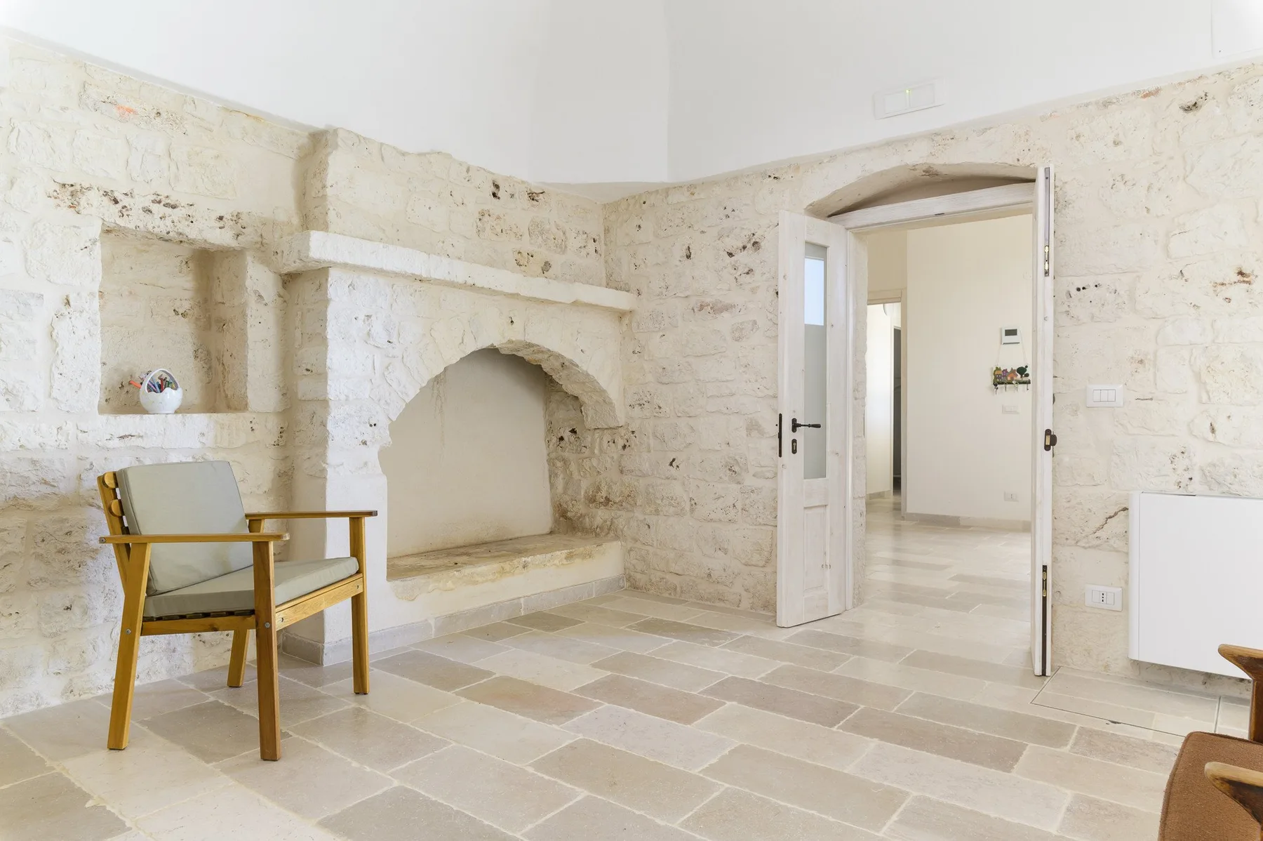 Una luminosa estancia de piedra con una silla de madera junto a un gran nicho arqueado.