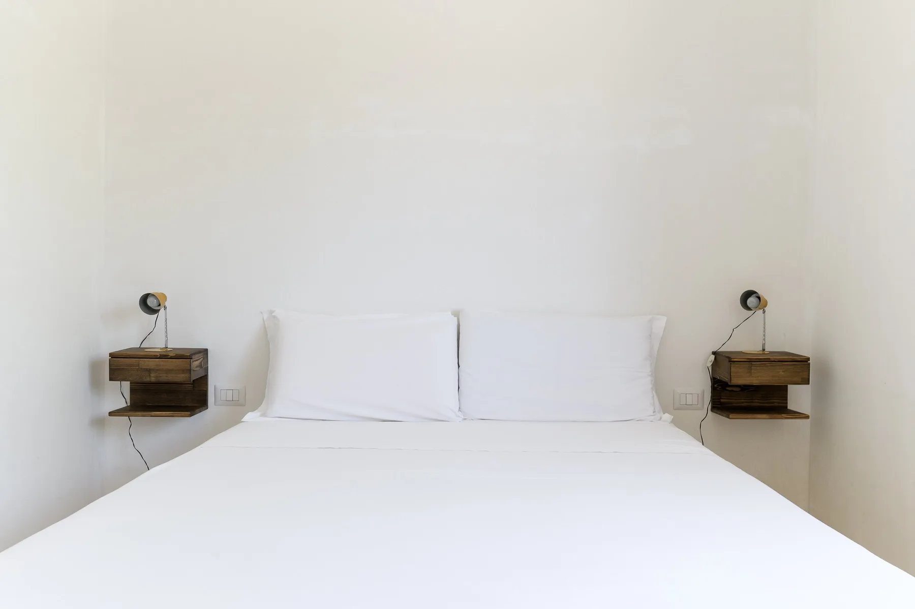 Un dormitorio con una cama tendida y estantes de noche montados en la pared.