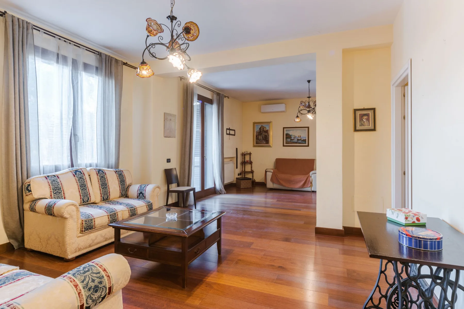 Una sala de estar con asientos estampados, una mesa de centro de vidrio y piso de madera.