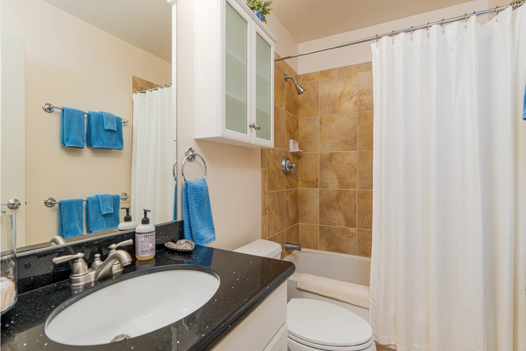 Un baño con tocador oscuro, lavabo y ducha revestida de azulejos detrás de una cortina blanca.