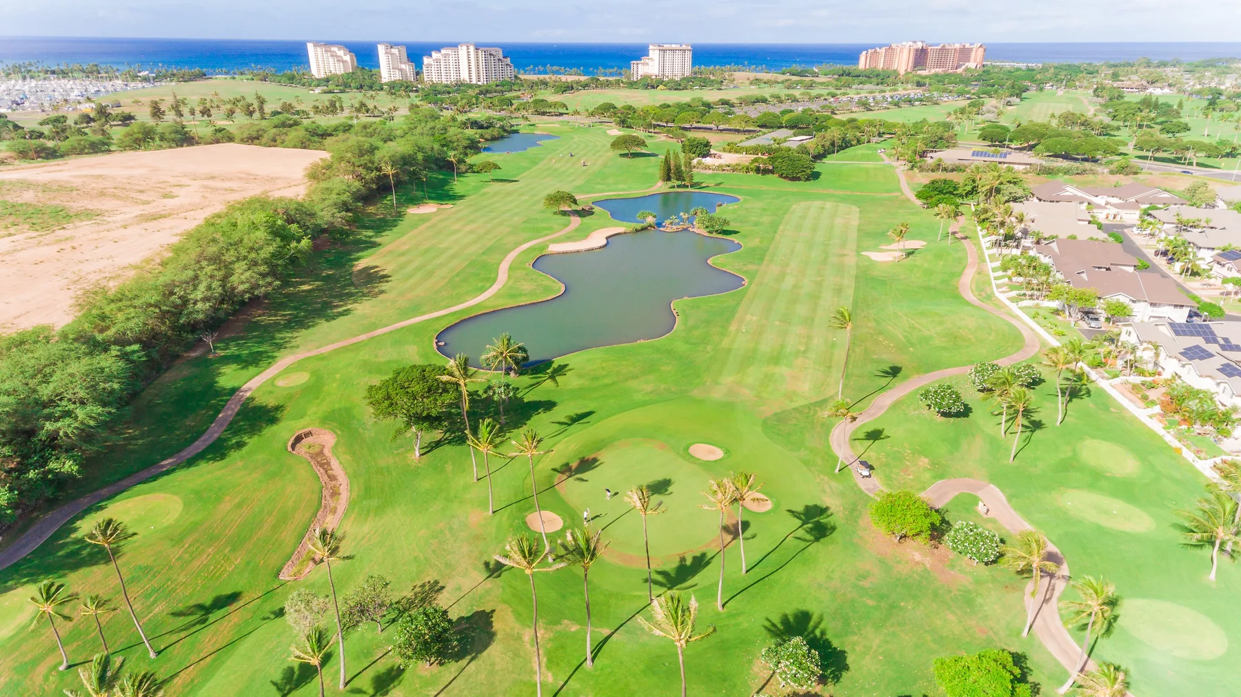 Vista aérea de un campo de golf verde con un estanque y el océano al fondo.