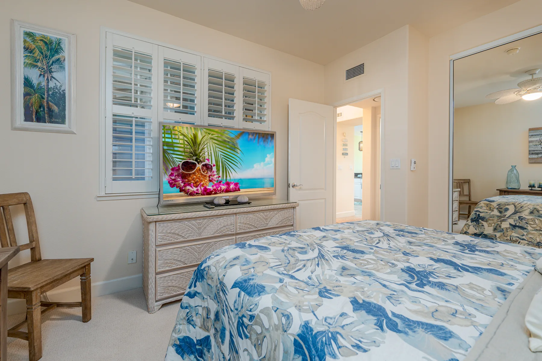 Un dormitorio con una cama, una cómoda y un televisor bajo ventanas con contraventanas.