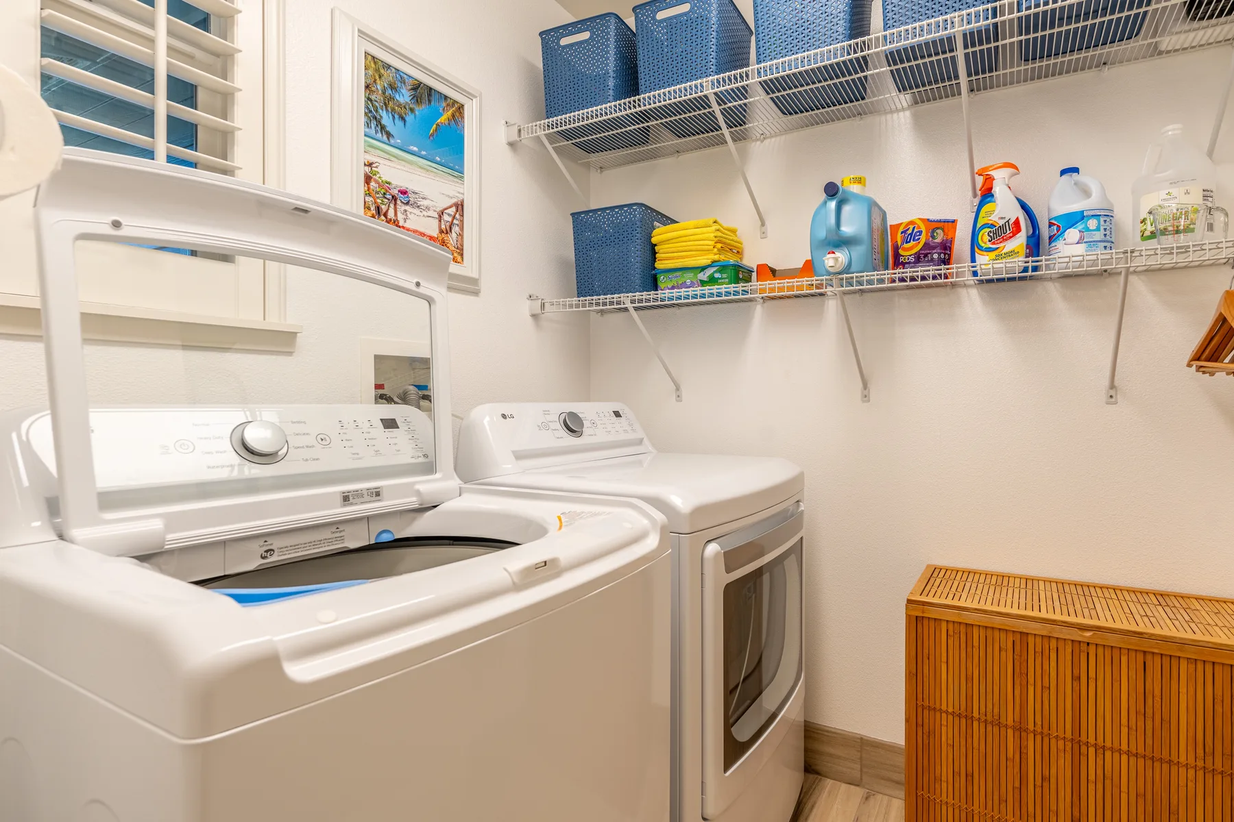 Un cuarto de lavandería con lavadora y secadora debajo de estantes con productos de limpieza.