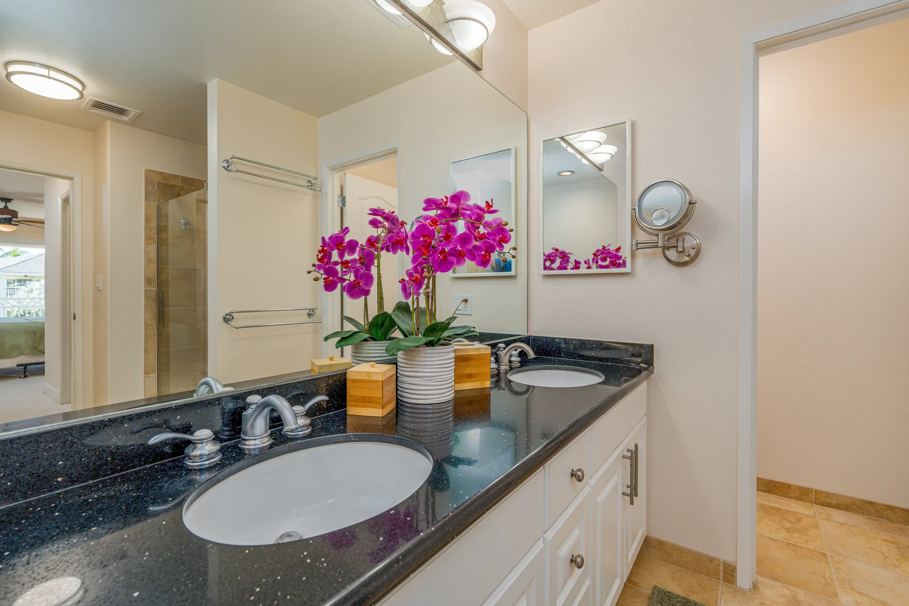 Un tocador de baño con encimera oscura, lavabo y orquídeas.