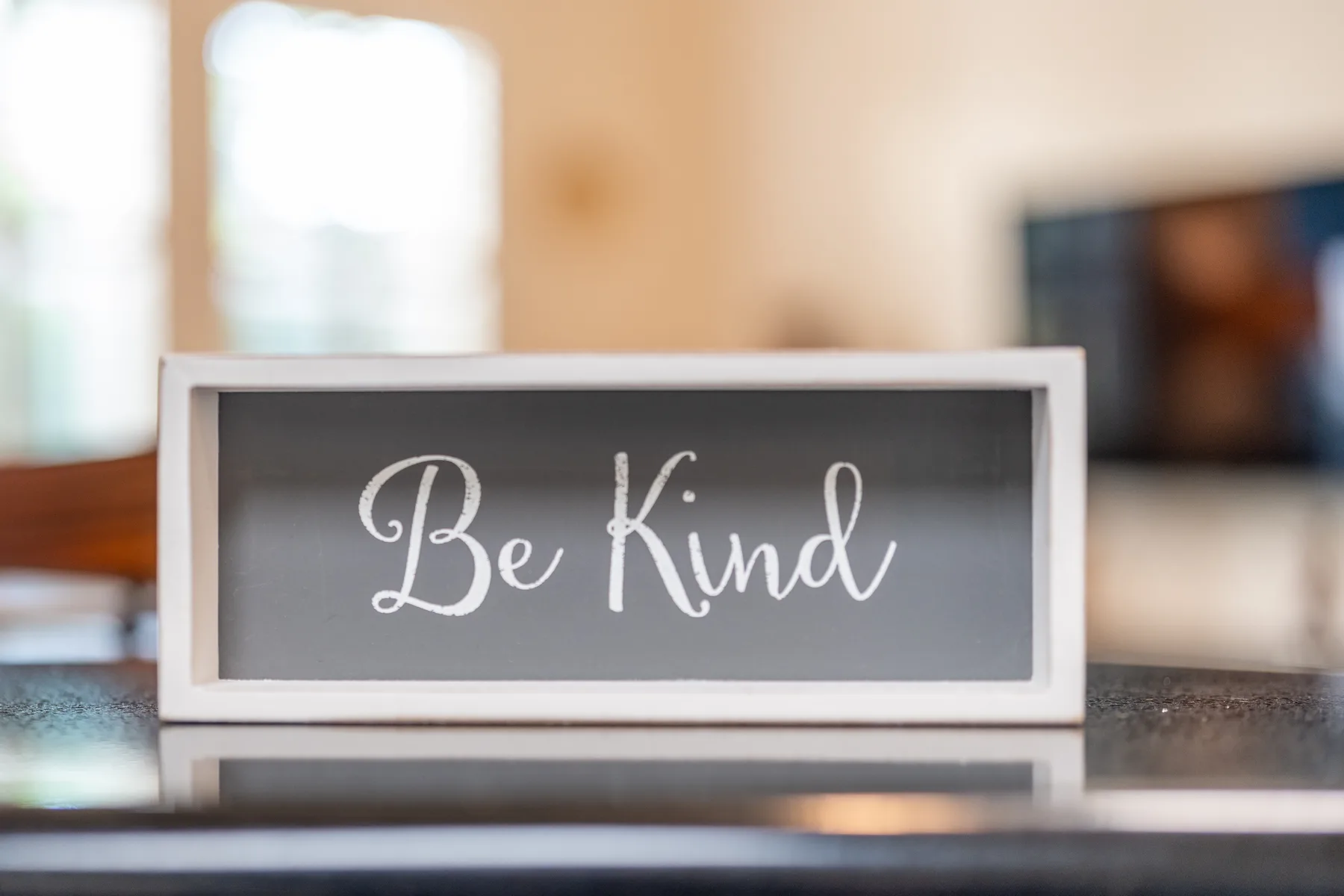 Un letrero de pizarra que dice «Be Kind» está sobre una encimera en un comedor.