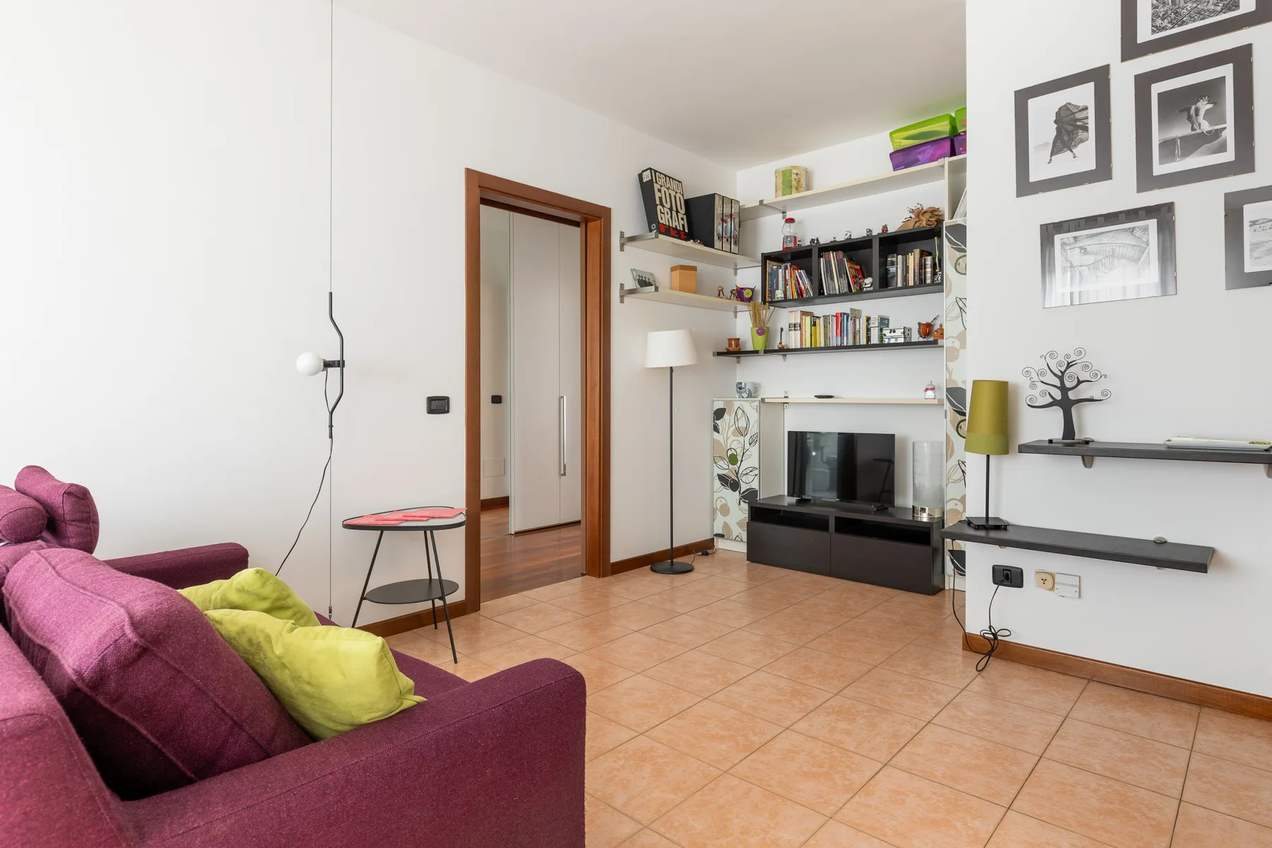 Una sala de estar con televisor, estantes en la pared y un sofá morado.