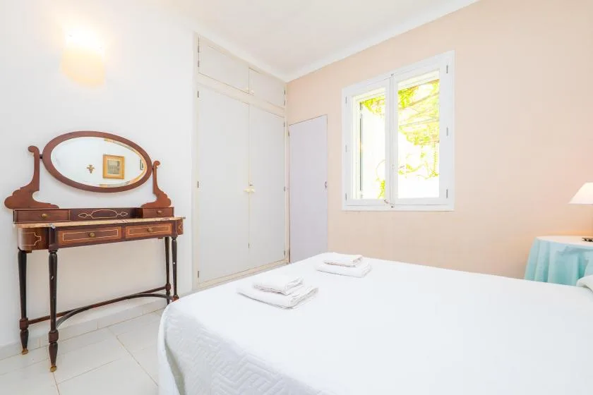 A bright bedroom with a neatly made bed and a window overlooking greenery.