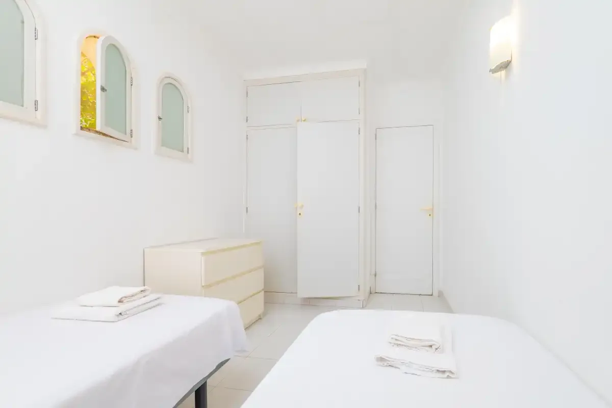 A bright bedroom with two beds and a white dresser.