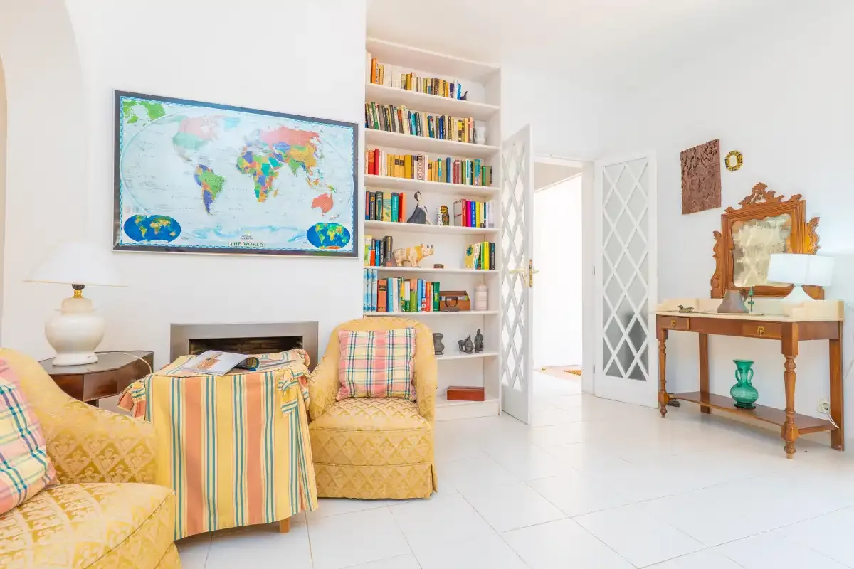 A bright sitting room with patterned seating, a bookshelf, and a map on the wall.