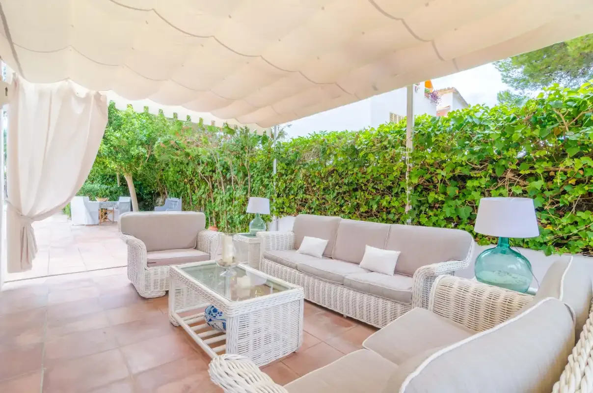 A covered outdoor seating area with wicker furniture and a glass coffee table.