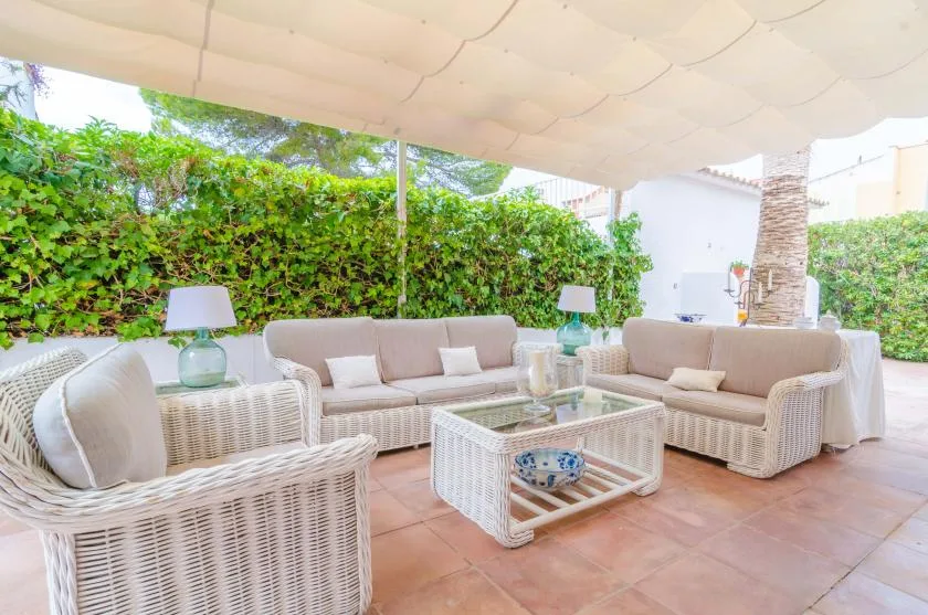 An outdoor seating area under a canopy, with wicker seating around a glass coffee table.