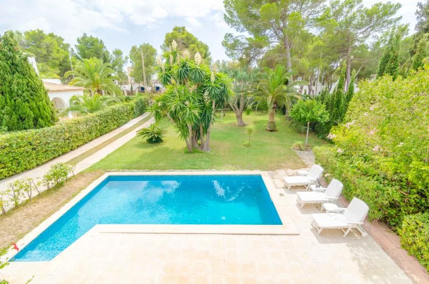 An outdoor swimming pool overlooks a landscaped garden with trees and lounge seating.