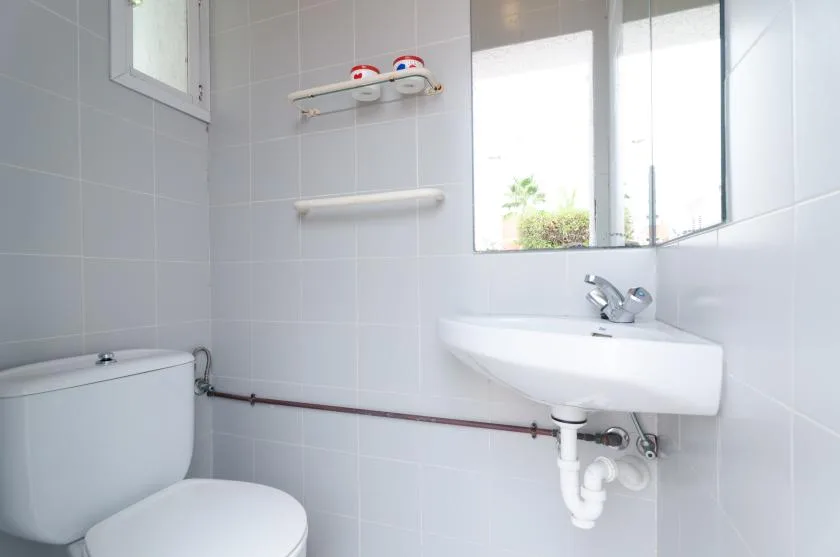 A tiled bathroom with a toilet and wall-mounted sink beneath a bright window.
