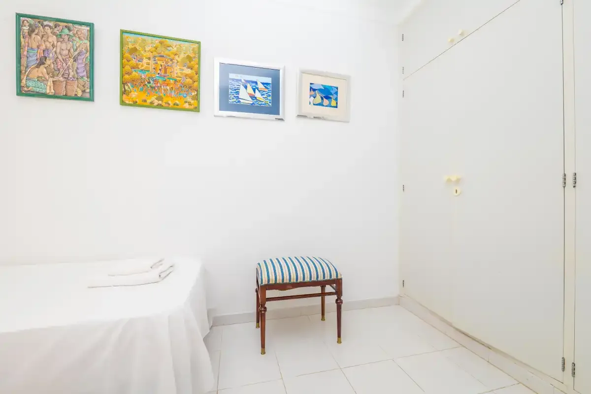 A bright bedroom with a bed, striped bench, and colorful framed artwork.