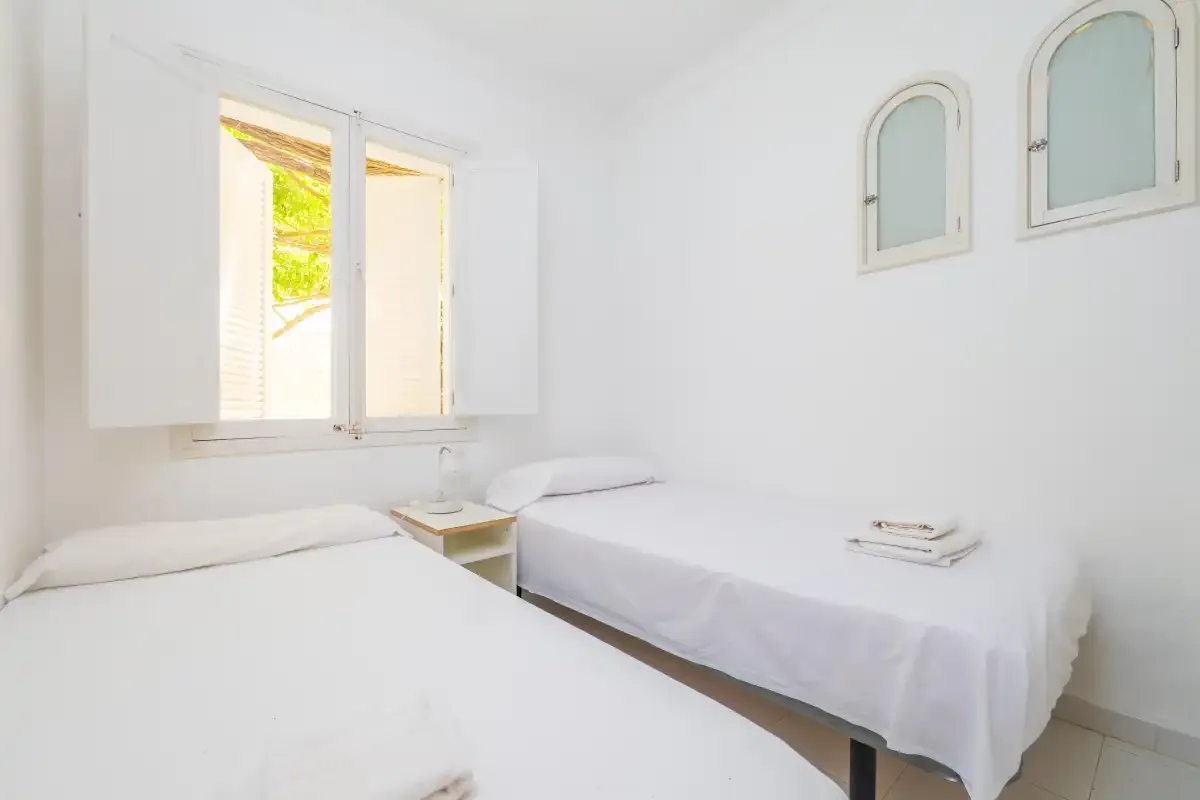 A bright bedroom with two beds and an open window.
