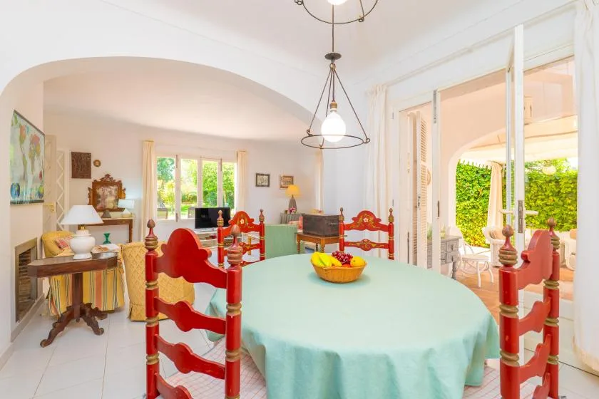 A dining room with a large table and red chairs, opening onto a bright patio.