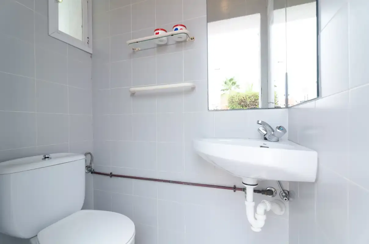 A tiled bathroom with a sink, toilet, and bright window.