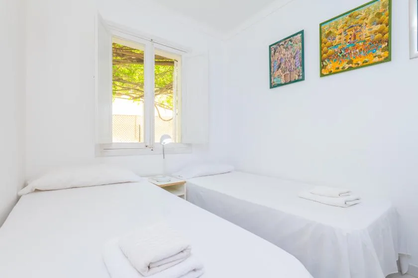 A bright bedroom has two single beds and colorful artwork on the walls.