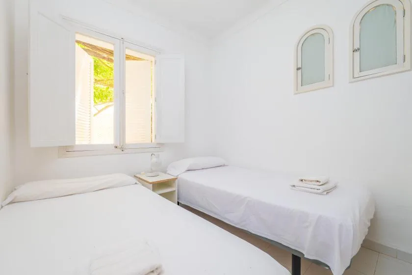 A bright bedroom with two single beds and an open window.