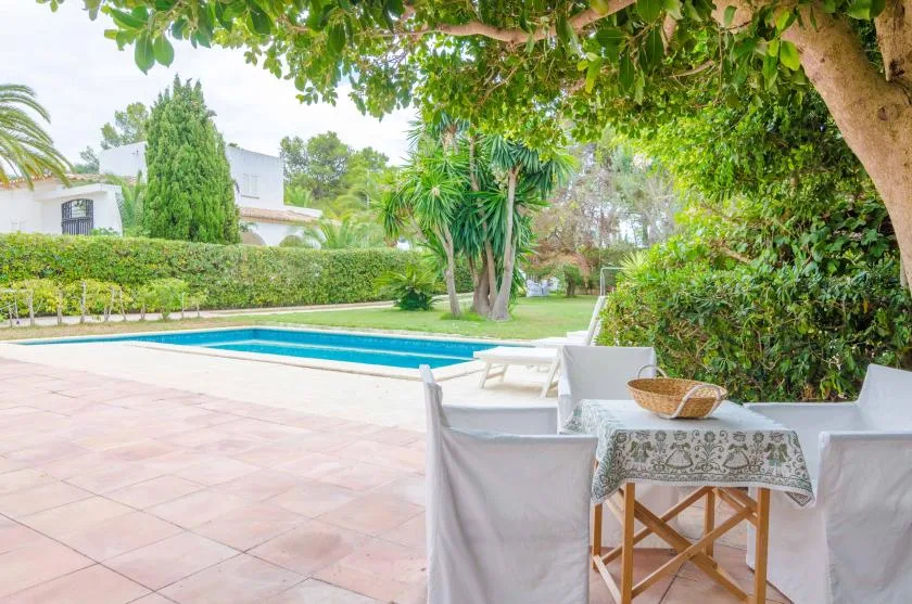 A garden patio dining area overlooks a swimming pool and landscaped greenery.