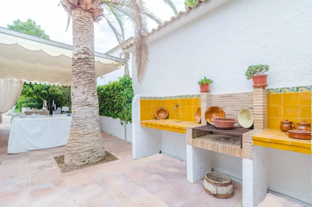 An outdoor patio with a tiled cooking counter and a shaded dining area.