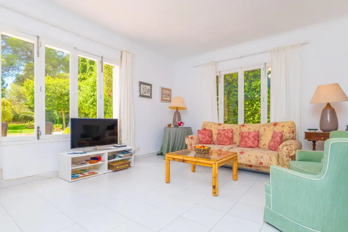 A bright living room with floral seating and large windows overlooking greenery.