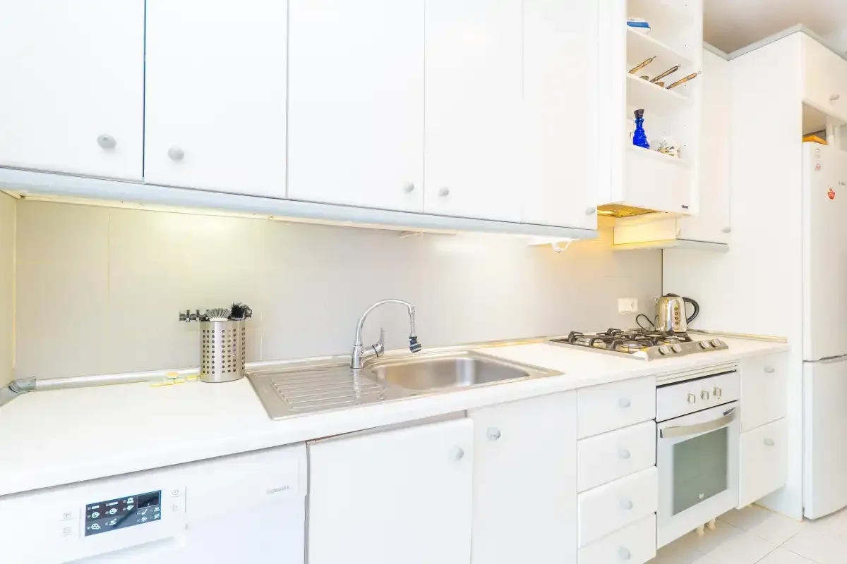 A bright kitchen with white cabinets, a sink, and a cooktop.