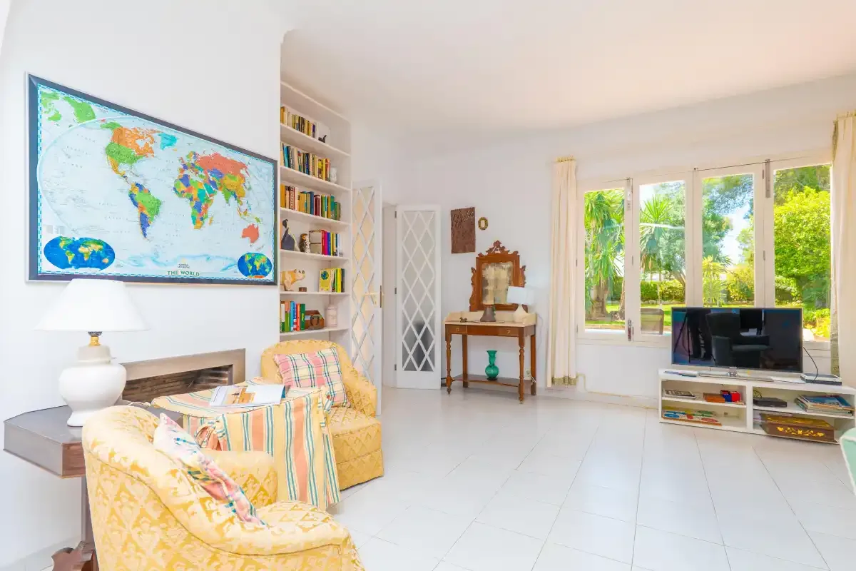 A bright living room with seating, bookshelves, and large windows overlooking greenery.