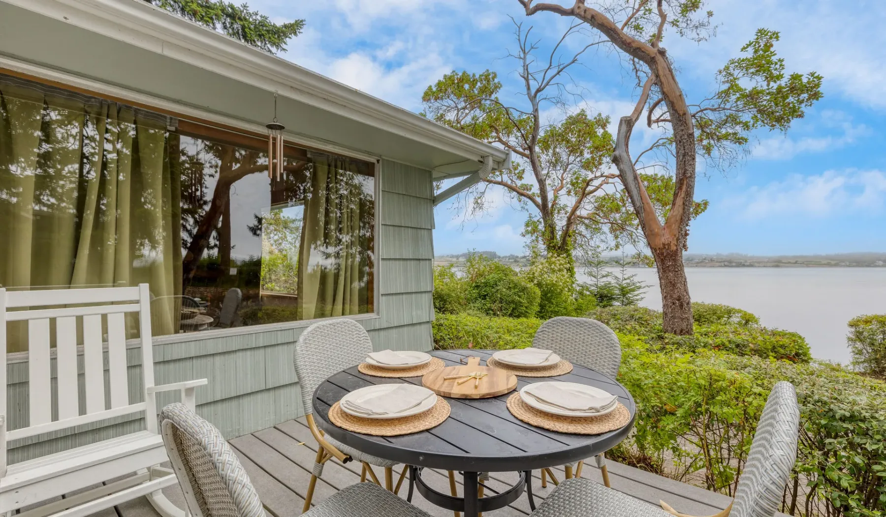 Una zona de comedor al aire libre junto a una casa tiene vistas al agua.