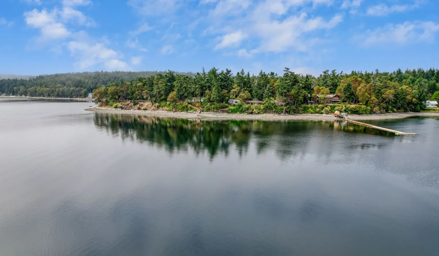 Un lago tranquilo refleja una orilla arbolada bajo un cielo parcialmente nublado.