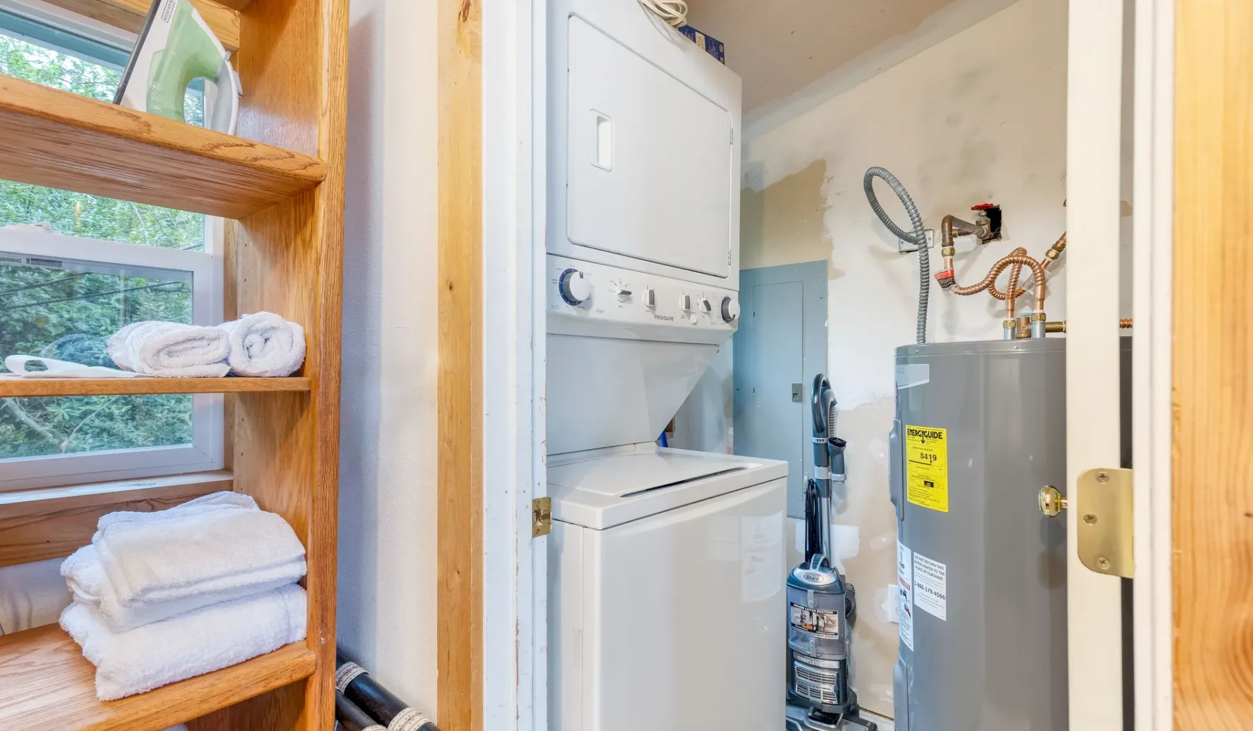 Zona de lavandería y servicio con electrodomésticos apilados y estantes con toallas dobladas.