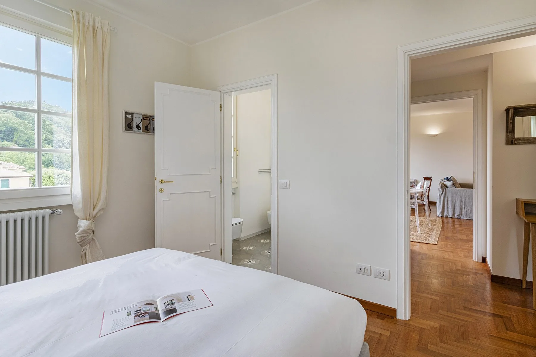 A bright bedroom with a large window, radiator, and doorway to a bathroom.