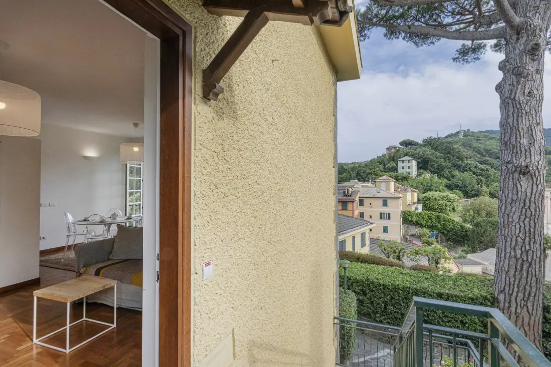 A balcony overlooks green hills and nearby buildings, with an open doorway to an interior room.