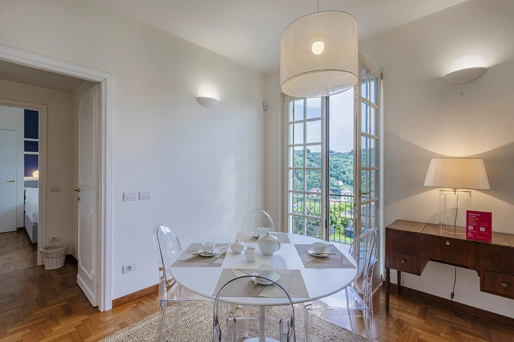 A bright dining area with a glass table beside open windows overlooking green hills.