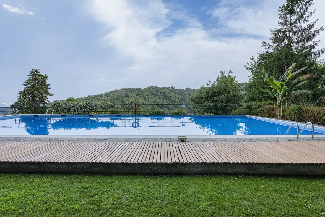 An outdoor swimming pool sits beside a wooden deck, with green hills in the distance.