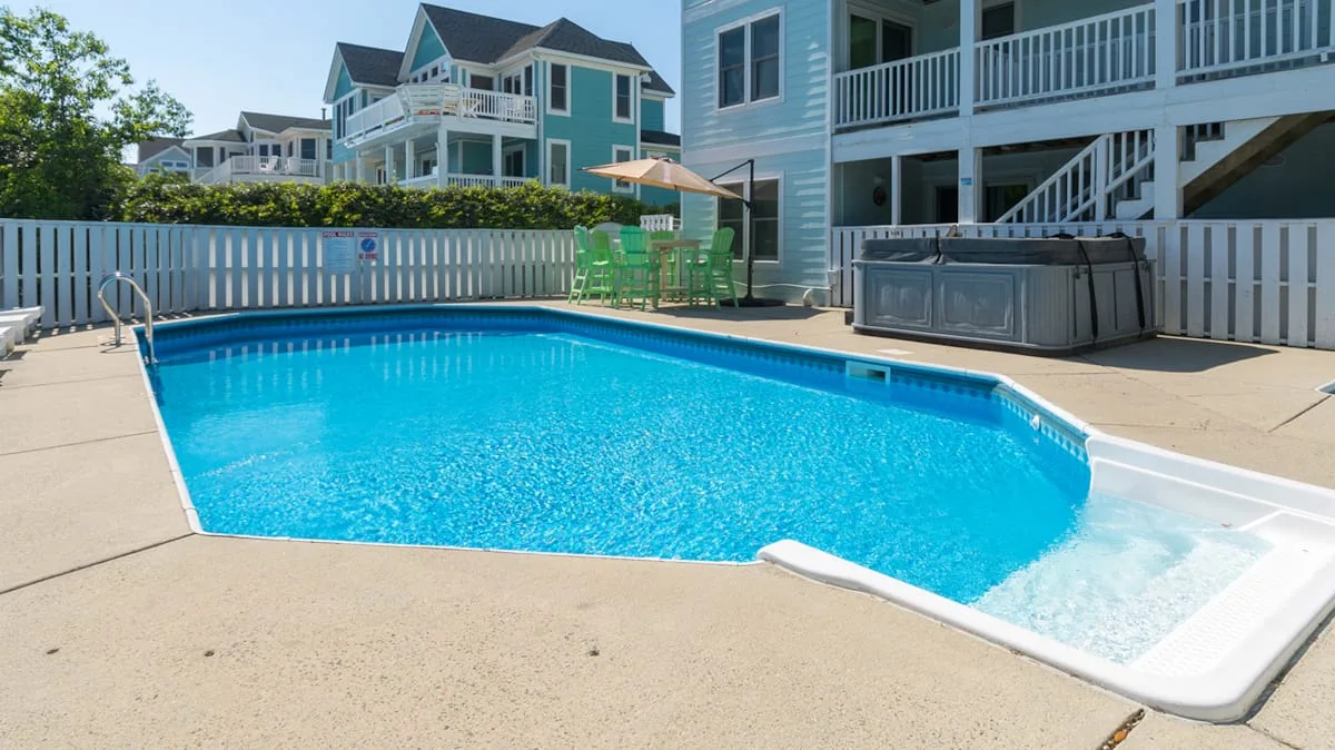 An outdoor swimming pool with a white fence and raised deck.