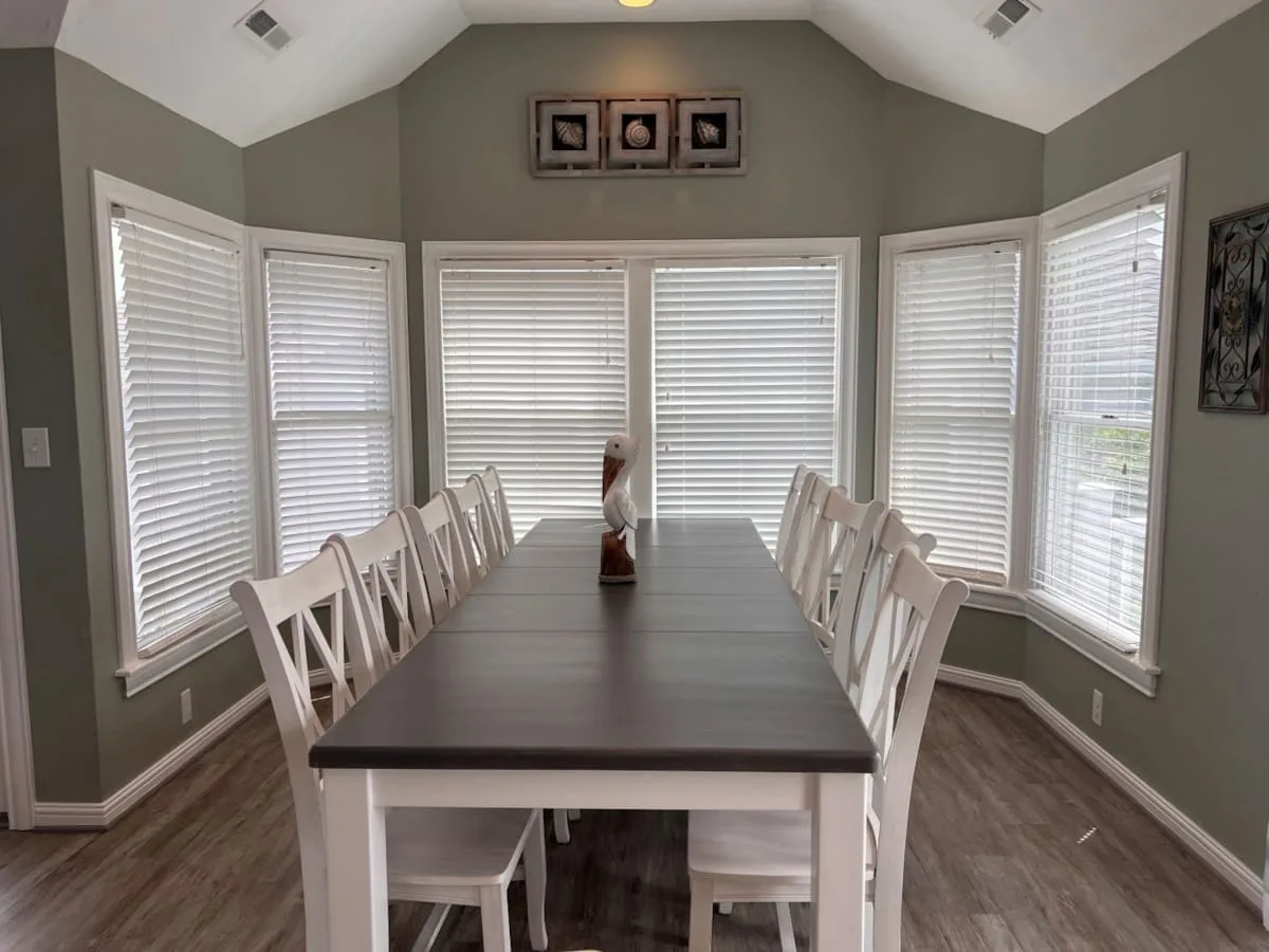 A dining room with a long table and seating beneath several windows.